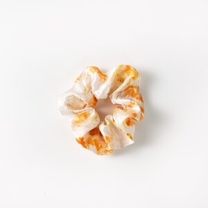 Puede incluir: Un scrunchie blanco con un patr&oacute;n de tie-dye naranja y amarillo.