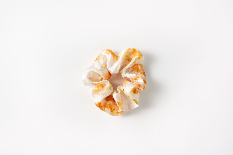 Puede incluir: Un scrunchie blanco con un patr&oacute;n de tie-dye naranja y amarillo.
