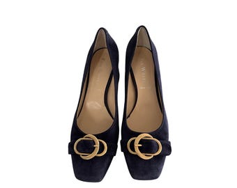 Könnte beinhalten: Ein Paar marineblaue Wildleder-Pumps mit quadratischer Spitze. Jeder Schuh hat eine goldfarbene Schnalle am Rist. Die Absätze sind moderat hoch und bieten einen klassischen und eleganten Look.