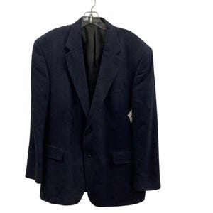 May include: A navy blue blazer hanging on a hanger. The blazer has a two-button closure, notched lapels, and two front pockets. The interior lining is black. The blazer is made of a textured fabric.