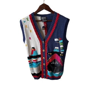 Könnte beinhalten: Eine Vintage-Weste ohne Ärmel mit nautischem Thema. Die Weste hat ein weißes und marineblaues Farbblockdesign mit rotem Besatz. Die Vorderseite hat goldene Knöpfe und ein detailliertes Strickdesign von Booten und Flaggen.