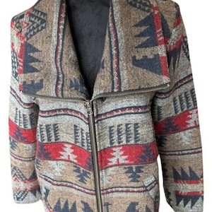 Könnte beinhalten: Gemusterte Jacke mit Reißverschluss. Die Jacke hat ein braunes, rotes und marineblaues geometrisches Design. Der Kragen ist breit und die Jacke wird auf einer schwarzen Schaufensterpuppe präsentiert.