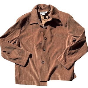 May include: A brown button-down jacket with a collared neckline. The jacket has long sleeves and a slightly textured appearance. The brand name "BRIGGS" is visible on the label. The jacket is made of a soft material.