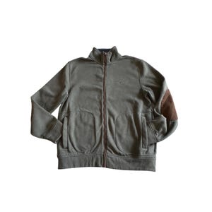 May include: Olive green zip-up jacket with a high collar and brown elbow patches. The jacket has two front pockets and a small logo on the chest. The zipper and pocket trim are a darker brown color.