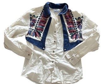 May include: Cream-colored button-down shirt with long sleeves. Features a denim collar and yoke with colorful feather-like embroidery. The shirt has silver buttons and a classic Western style.