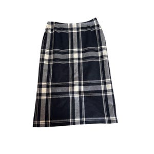 May include: A navy blue, white, and grey plaid skirt. The skirt is knee-length and has a straight cut. The fabric is woven, and the plaid pattern is a grid of intersecting lines. The skirt is a classic design.