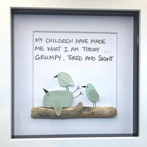 Può includere: Opera d'arte incorniciata con tre uccelli in vetro marino appollaiati su un ramo di legno. Il testo recita: "MY CHILDREN HAVE MADE ME WHAT I AM TODAY... GRUMPY, TIRED AND SKINT."