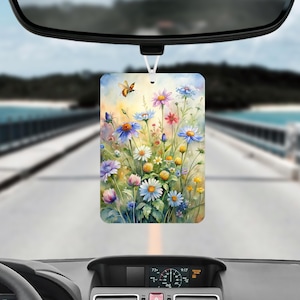 May include: Rectangular car air freshener featuring a watercolor painting of colorful wildflowers and a bee. The design includes blue, purple, pink, and yellow flowers. The air freshener hangs from a white string.