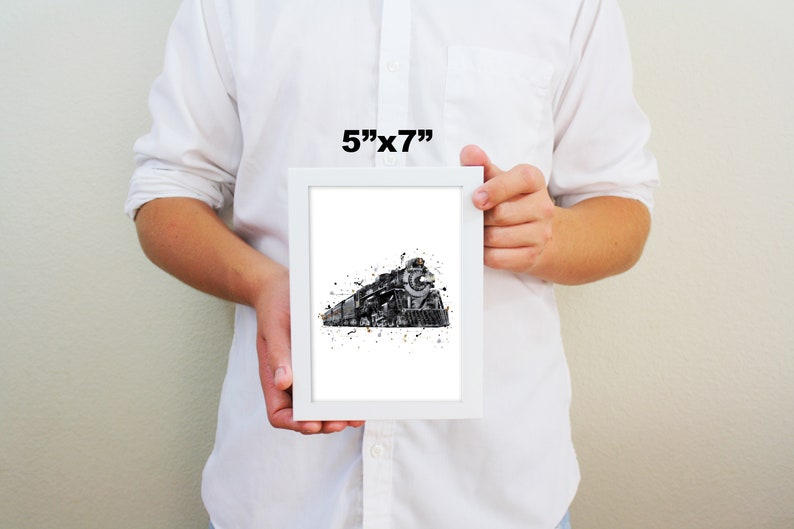 May include: A framed black and white watercolor print of a vintage steam locomotive with gold accents. The print is 5 inches by 7 inches and is framed in a white frame.