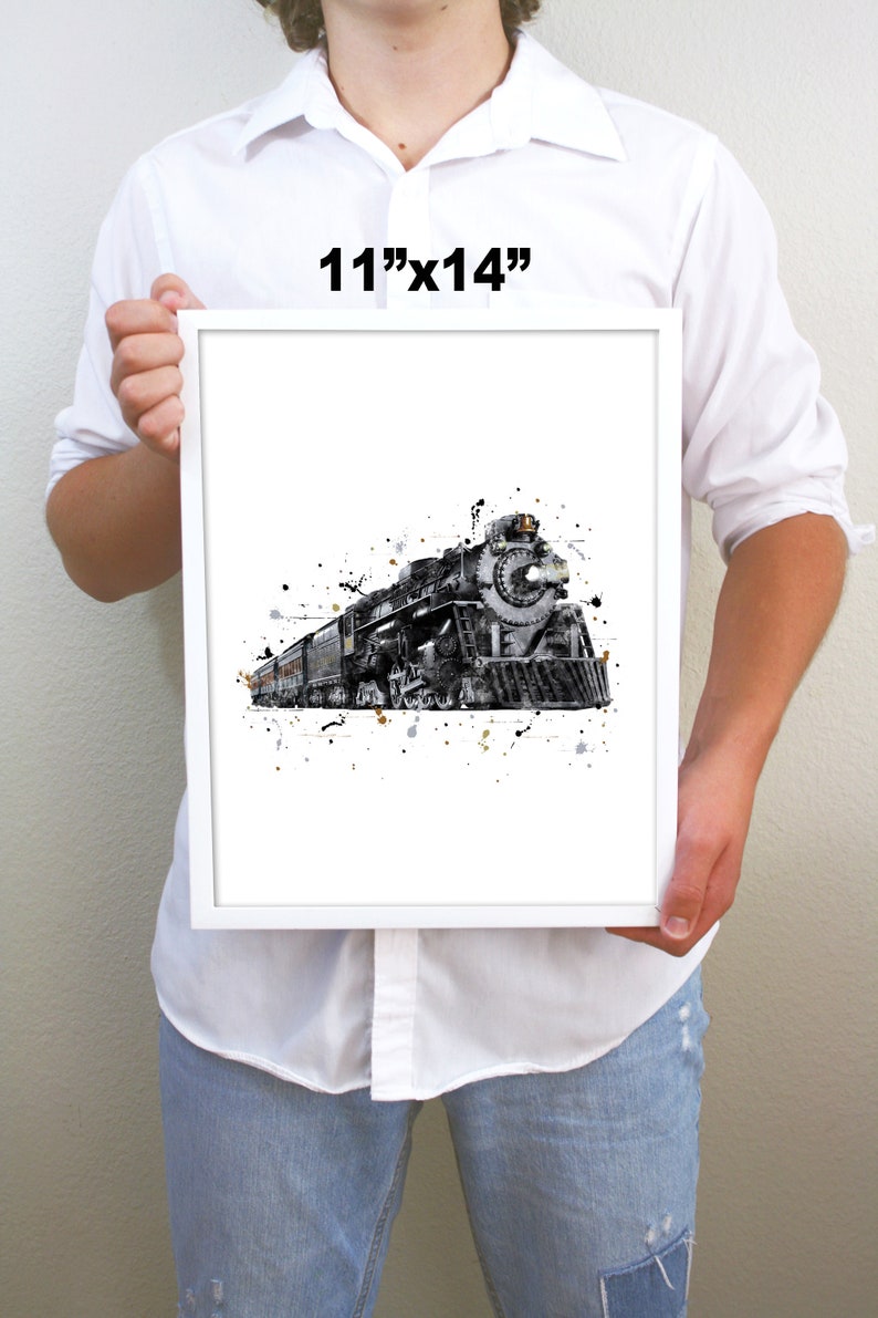 May include: A black and white watercolor print of a vintage steam locomotive train with gold and gray splatters on a white background. The print is framed in a white frame and measures 11 inches by 14 inches.