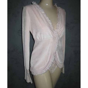 May include: A pale pink long-sleeved top with a ruffled neckline and a lace trim at the bottom.