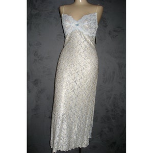 May include: A long, ivory-colored slip dress with a delicate lace overlay. The bodice features a light blue lace trim and a small bow detail. The dress has thin spaghetti straps and a flowing, floor-length skirt.