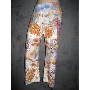May include: Lightweight lounge pants featuring a vibrant, multi-colored paisley and geometric pattern in shades of orange, yellow, pink, and blue on a cream background. The pants include a light blue elastic waistband with a matching drawstring tie.