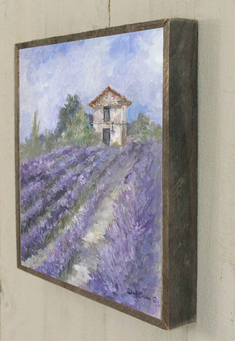 May include: A framed painting of a small white house with a red roof in a field of lavender. The painting is signed "D. Cruise" in the bottom right corner.