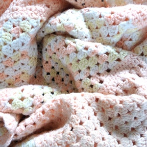 May include: A crocheted baby blanket in shades of pink, white, and yellow. The blanket is made with a granny square pattern.