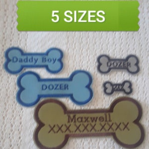 May include: Five dog bone-shaped patches in different sizes and colors. The patches are embroidered with the names "Daddy Boy", "Dozer", "Maxwel", and "Dozer" in different fonts.