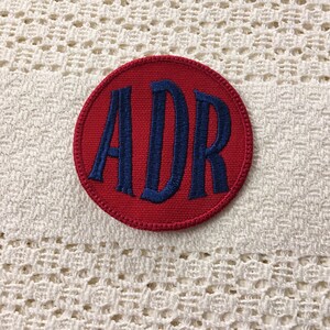 Peut inclure: Patch circulaire rouge avec des lettres brodées bleues épellées "ADR".