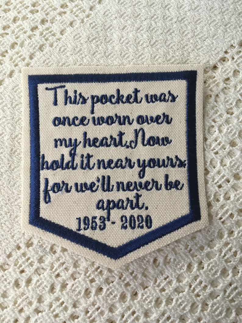 May include: A white fabric patch with blue embroidered text that reads "This pocket was once worn over my heart. Now hold it near yours for we'll never be apart. 1953-2020".