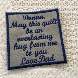 May include: A gray fabric patch with blue embroidered text that reads "Donna, May this quilt be an everlasting hug from me to you. Love, Dad."