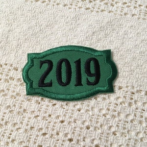 May include: A green fabric patch with a white border and the year 2019 embroidered in black.