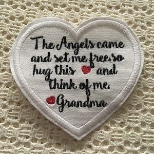 May include: White heart-shaped fabric patch with embroidered text: "The Angels came and set me free so hug this and think of me Grandma". Two red hearts are embroidered on the patch.