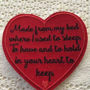 May include: Red felt heart-shaped patch with black embroidered text that reads "Made from my bed where I used to sleep, To have and to hold in your heart to keep."