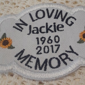 Può includere: Toppa bianca ricamata a forma di nuvola con il testo "In Loving Memory Jackie 1960 2017". Due girasoli ricamati gialli si trovano su entrambi i lati del testo.