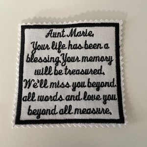 Puede incluir: Parche de tela blanca con texto bordado en negro que dice "Aunt Marie, Your life has been a blessing. Your memory will be treasured. We'll miss you beyond all words and love you beyond all measure."
