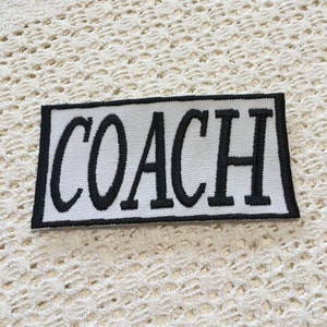 May include: White patch with black embroidered text that reads "COACH".