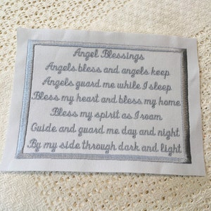 Może przedstawiać: Biały kwadratowy kawałek materiału z srebrną haftowaną ramką i tekstem "Angel Blessings Angels bless and angels keep Angels guard me while I sleep Bless my heart and bless my home Bless my spirit as I roam Guide and guard me day and night By my side through dark and light"