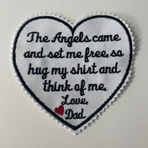 May include: White heart-shaped patch with black stitching and the text "The Angels came and set me free, so hug my shirt and think of me Love, Dad" with a small red heart.