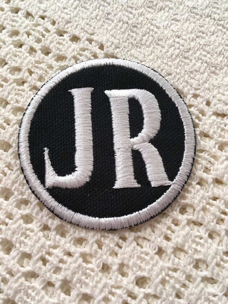 Pu&ograve; includere: Una toppa ricamata in bianco e nero con le lettere "JR" in un cerchio.
