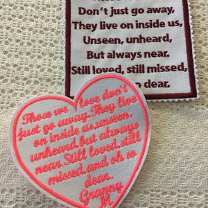 Op de afbeelding: Twee witte stoffen patches met roze stiksels. De bovenste patch heeft een donkerrode rand en de tekst "Those we love Don't just go away, They live on inside us, Unseen, unheard, But always near. Still loved, still missed, dear." De onderste patch is hartvormig en heeft de tekst "Those we love don't just go away. They live on inside us unseen, unheard, but always near. Still loved, still missed, and oh so dear. Granny M."