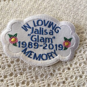 May include: White embroidered patch with blue text that reads "In Loving Memory Jalisia "Glam" 1989-2019". The patch has two pink flowers with green leaves on each side.