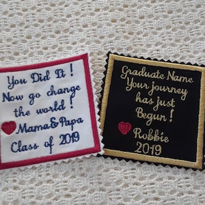 May include: Two graduation patches, one white with red trim and the other black with gold trim. The white patch says "You Did It! Now go change the world! Mama & Papa Class of 2019" with a red heart. The black patch says "Graduate Name Your journey has just Begun! Robbie 2019" with a red heart.