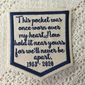 May include: A white fabric patch with blue embroidered text that reads "This pocket was once worn over my heart. Now hold it near yours for we'll never be apart. 1953-2020".