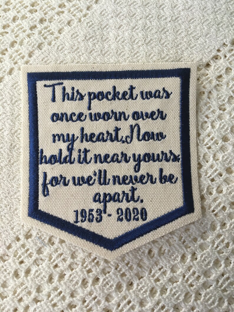 May include: A white fabric patch with blue embroidered text that reads "This pocket was once worn over my heart. Now hold it near yours for we'll never be apart. 1953-2020".