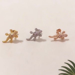 Può includere: Tre orecchini a forma di lucertola in oro, argento e oro rosa, ognuno con strass trasparenti. Gli orecchini sono presentati su uno sfondo bianco.
