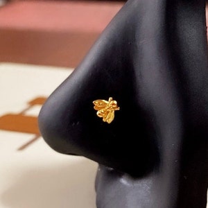 May include: A gold nose ring with a bee design. The bee is detailed with wings, legs, and a body.