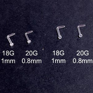 May include: Four clear, L-shaped nose studs are displayed on a black surface. Two are 18G with 1mm diameter, and two are 20G with 0.8mm diameter. The text on the image indicates the gauge and diameter of each stud.