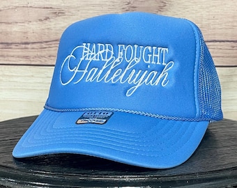 May include: A blue trucker hat with white embroidered text that reads "Hard Fought Hallelujah".