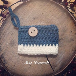 May include: A blue and white crocheted coin purse with a wooden button. The purse is sitting on a wooden surface.