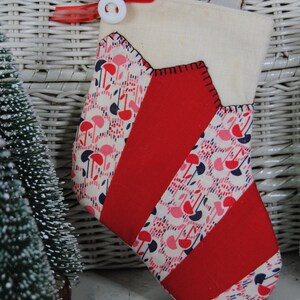 May include: A red and white striped Christmas stocking with a pink and blue floral pattern. The stocking has a white cuff and a white button.