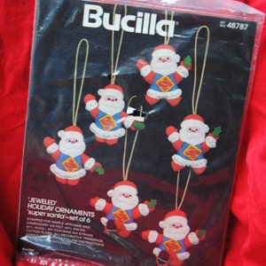 May include: A Bucilla kit for making six "Super Santa" holiday ornaments. The ornaments feature Santa Claus in a Superman costume. The kit includes stamped felt, embroidery floss, decorative trimmings, and instructions.