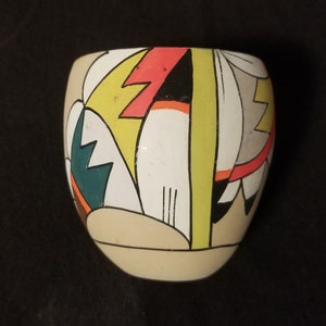 May include: A small, round, ceramic pot with a geometric design in shades of yellow, red, white, black, and green.