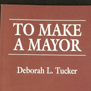 May include: A burgundy book with the title "To Make A Mayor" by Deborah L. Tucker. The book is published by the University Press of America.