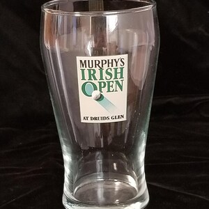 Op de afbeelding: Een helder pintglas met een uitlopende vorm. Het glas heeft de tekst "Murphy's Irish Open" in groen en wit, met een golfbalafbeelding. De tekst "At Druids Glen" staat eronder.