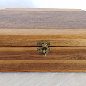 May include: A wooden box with a hinged lid and a brass latch. The box is made of light and dark wood and has a rectangular shape.