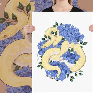 以下が含まれることがあります： 青いアジサイの花と白いヘビ。ヘビは画像の中央に丸まっていて、花はヘビの周りに配置されています。画像の下部に「Starry Paige」というテキストがあります。