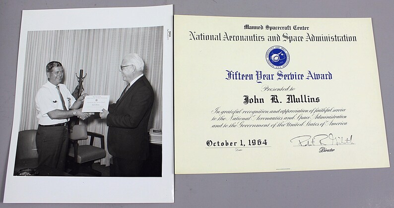 Pu&ograve; includere: Fotografia in bianco e nero di due uomini, uno dei quali consegna un certificato all'altro. Il certificato &egrave; un "Fifteen Year Service Award" della National Aeronautics and Space Administration, datato 1 ottobre 1964.